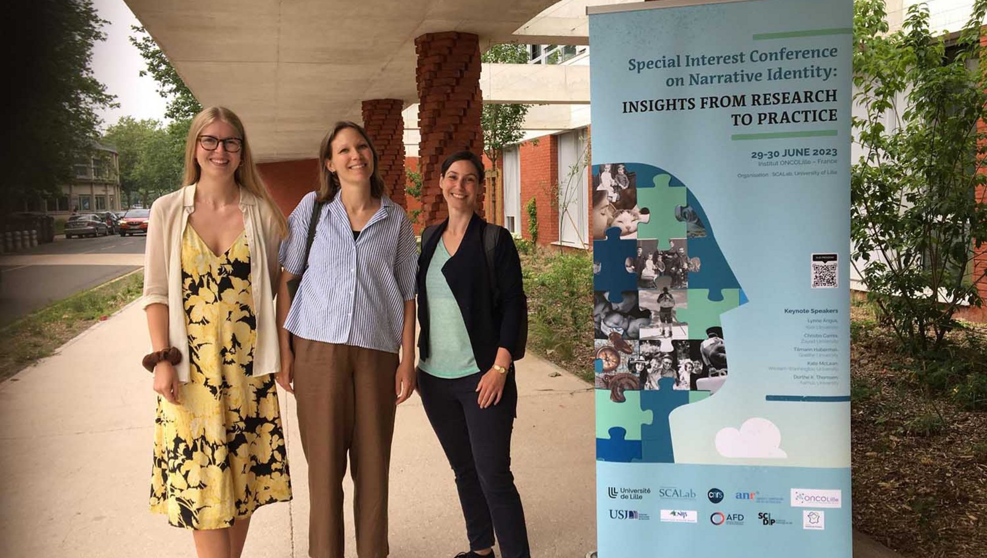 Tre personer fra The life story group står foran plakat for konference i Lille i Frankrig