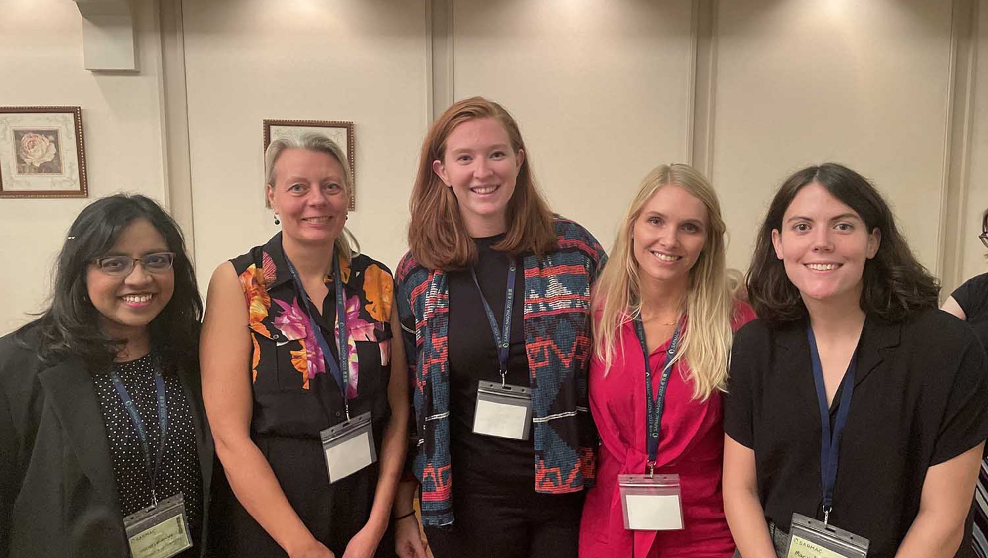 Fem kvinder står side om side og smiler til kameraet. De har skilte om halsen og deltager i SARMAC symposium.